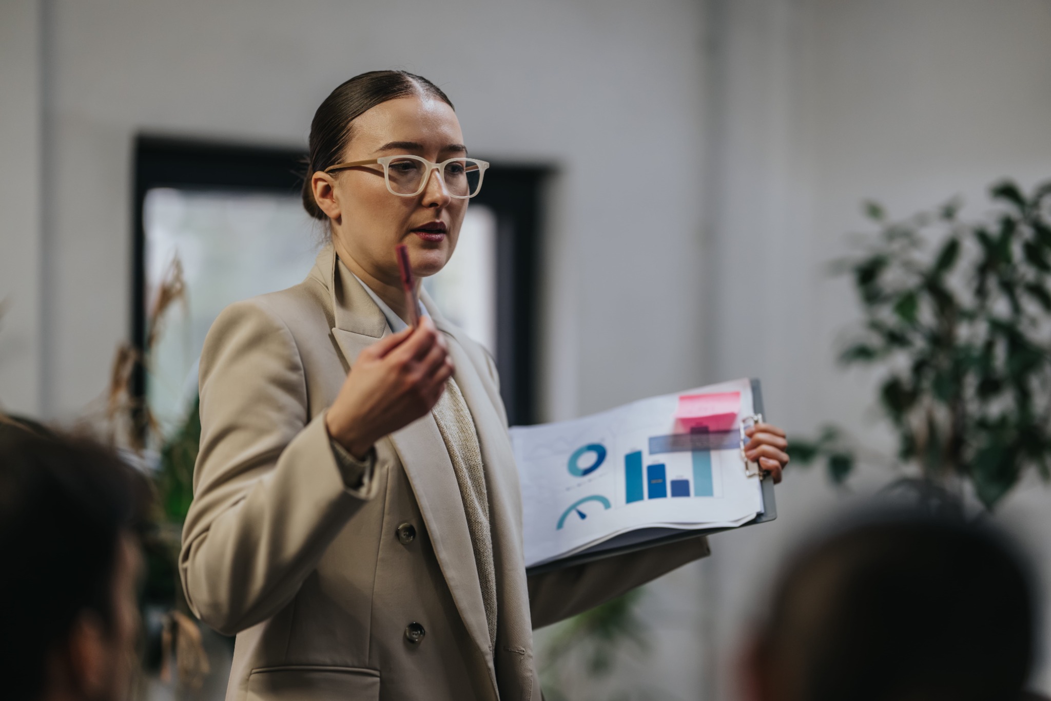 A presenter in a beige blazer holding project charts